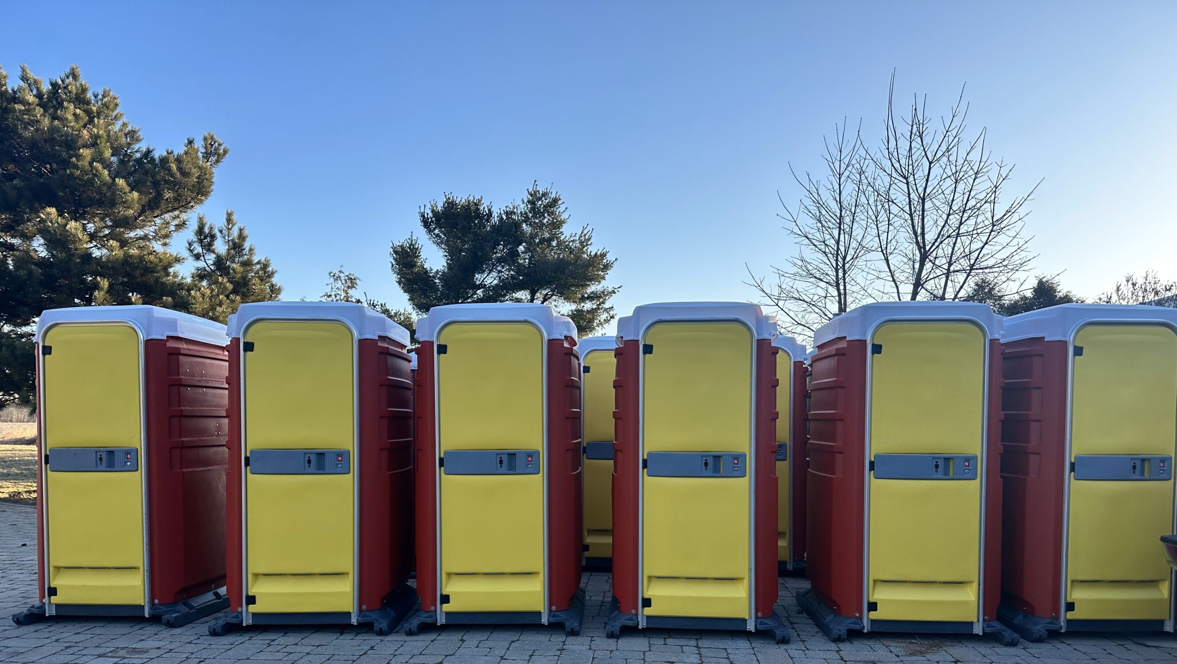 A row of portable toilets in front of trees.